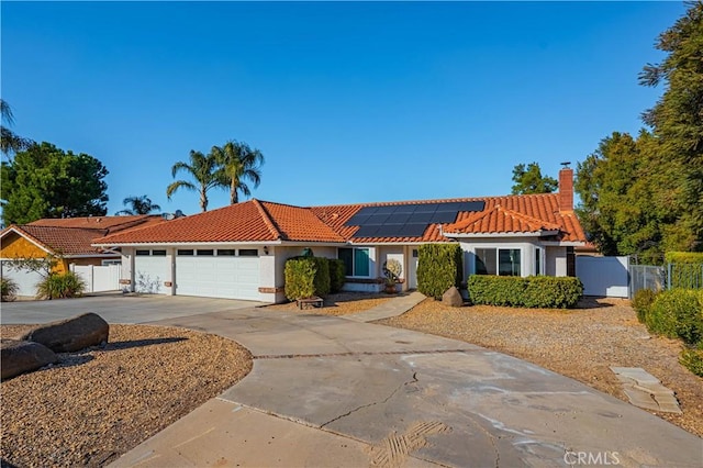 mediterranean / spanish-style home featuring solar panels, concrete driveway, a tile roof, and fence