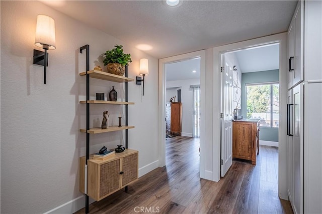 hallway with dark wood-type flooring, baseboards, and a textured ceiling