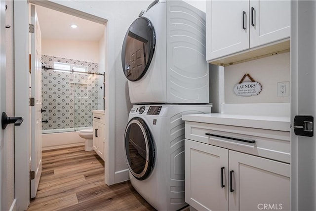 washroom featuring light wood-style flooring, cabinet space, and stacked washer / drying machine