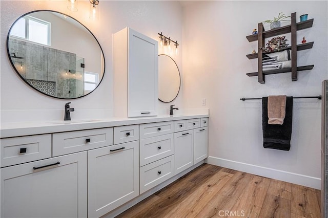 full bathroom with wood finished floors, baseboards, a tile shower, and a sink