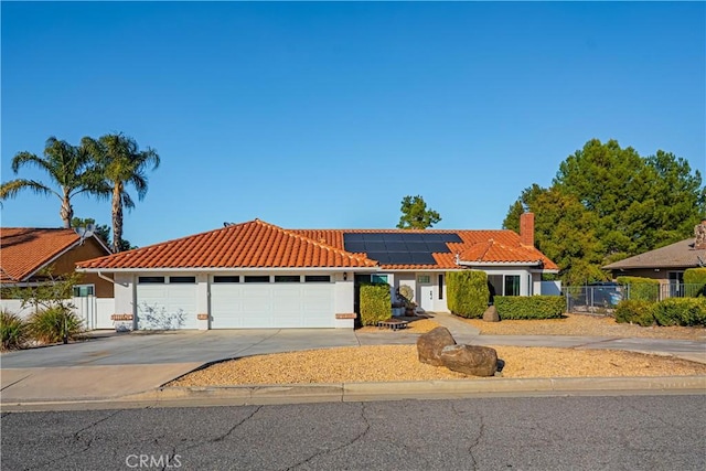 mediterranean / spanish house featuring fence, a tile roof, roof mounted solar panels, a garage, and driveway