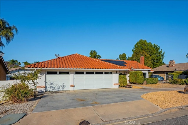 view of front of house with concrete driveway, a tile roof, roof mounted solar panels, stucco siding, and a garage