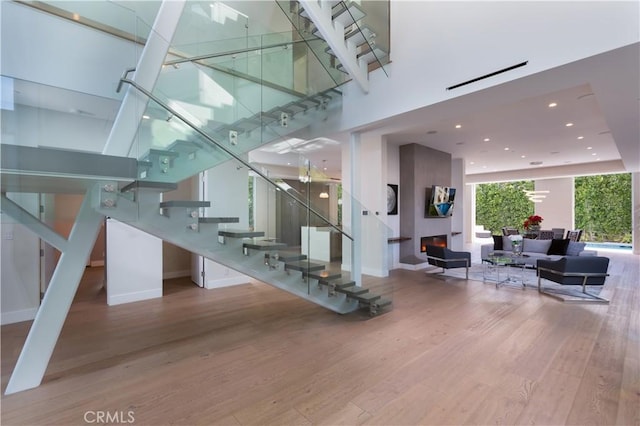 stairway with recessed lighting, baseboards, a warm lit fireplace, and wood finished floors