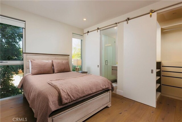 bedroom with recessed lighting, a barn door, ensuite bath, and wood finished floors