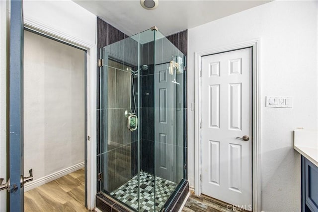 full bath with a stall shower, vanity, baseboards, and wood finished floors