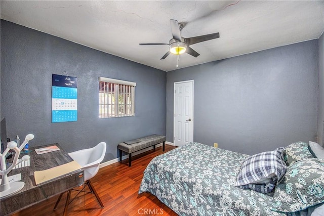 bedroom featuring a textured wall, ceiling fan, baseboards, and wood finished floors