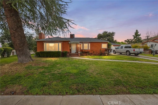 single story home with stucco siding, driveway, a chimney, and a front lawn