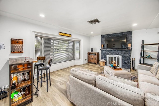 living area with visible vents, baseboards, a stone fireplace, recessed lighting, and light wood-style flooring