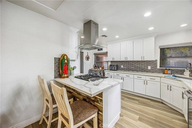 kitchen with light stone counters, light wood-style floors, tasteful backsplash, and island range hood