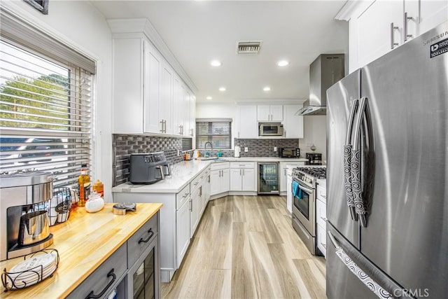 kitchen featuring wine cooler, decorative backsplash, white cabinets, stainless steel appliances, and wall chimney exhaust hood