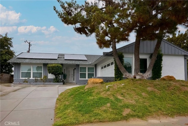 view of front facade with board and batten siding, a front yard, solar panels, a garage, and a shingled roof