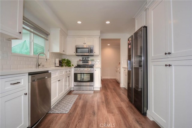 kitchen with light countertops, wood finished floors, appliances with stainless steel finishes, white cabinetry, and a sink