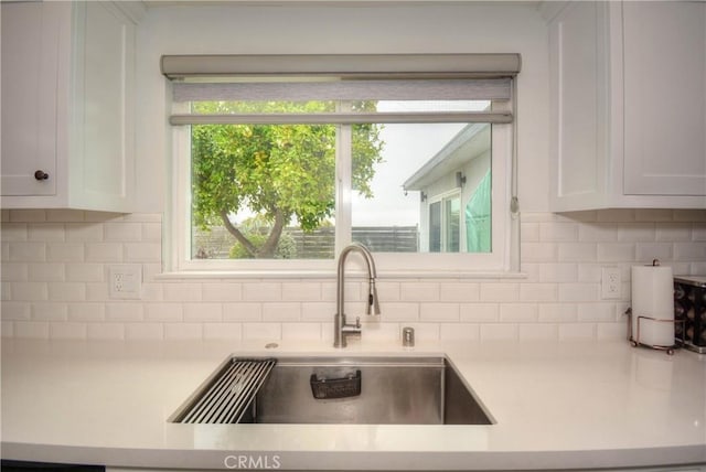 kitchen with white cabinetry, light countertops, a sink, and tasteful backsplash