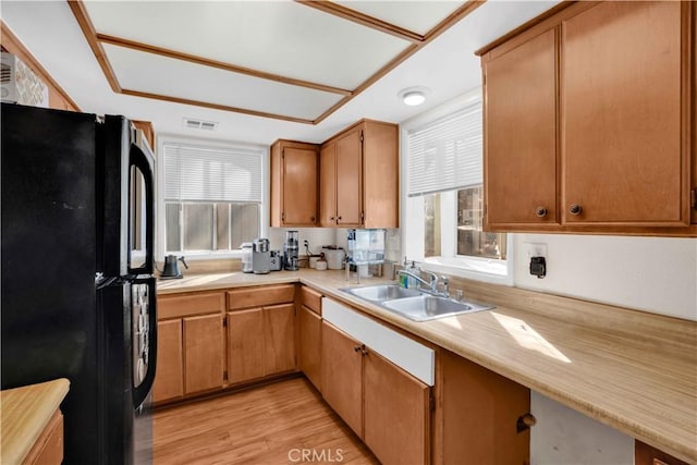 kitchen with visible vents, light countertops, light wood-style flooring, freestanding refrigerator, and a sink