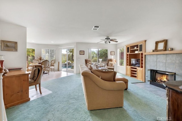 carpeted living area featuring tile patterned flooring, visible vents, a fireplace, and a ceiling fan