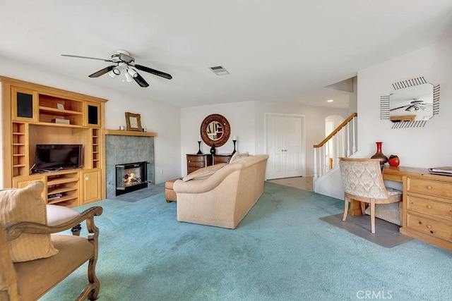 carpeted living room with stairway, a tile fireplace, visible vents, and ceiling fan