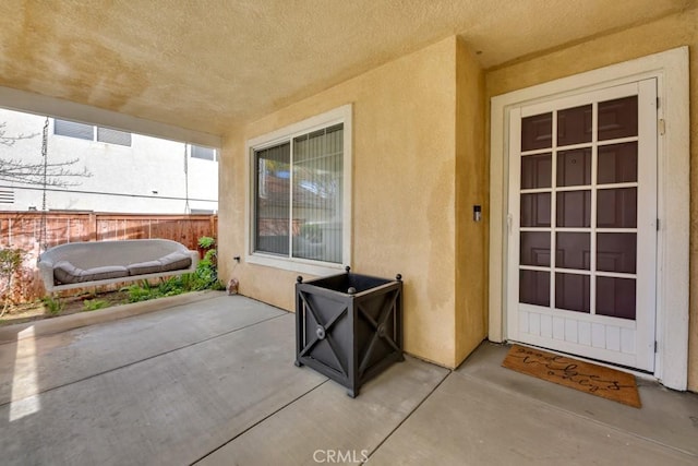 property entrance with stucco siding, a patio area, and fence