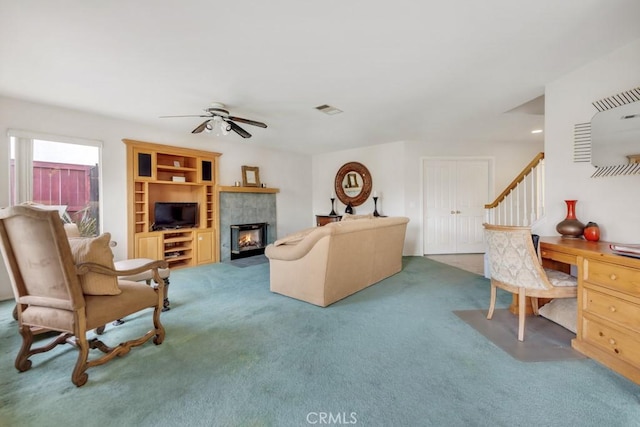 living area with a tiled fireplace, visible vents, carpet, and a ceiling fan