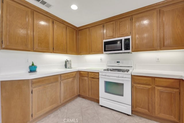 kitchen featuring visible vents, white appliances, brown cabinetry, and light countertops