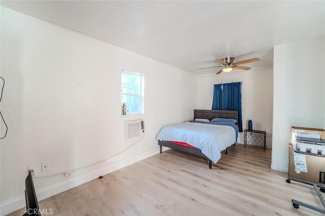 bedroom featuring baseboards, a wall mounted AC, light wood-style floors, and a ceiling fan