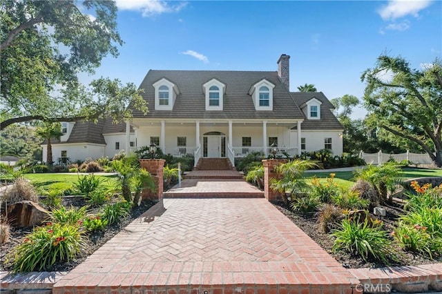 cape cod home with covered porch, a chimney, and fence