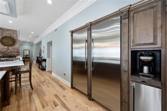 kitchen featuring dark brown cabinets, light wood-style floors, stainless steel built in fridge, and ornamental molding