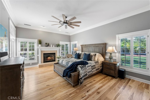 bedroom with a glass covered fireplace, crown molding, baseboards, and light wood finished floors