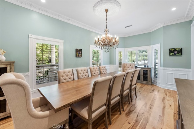 dining room with visible vents, a notable chandelier, ornamental molding, wainscoting, and light wood finished floors