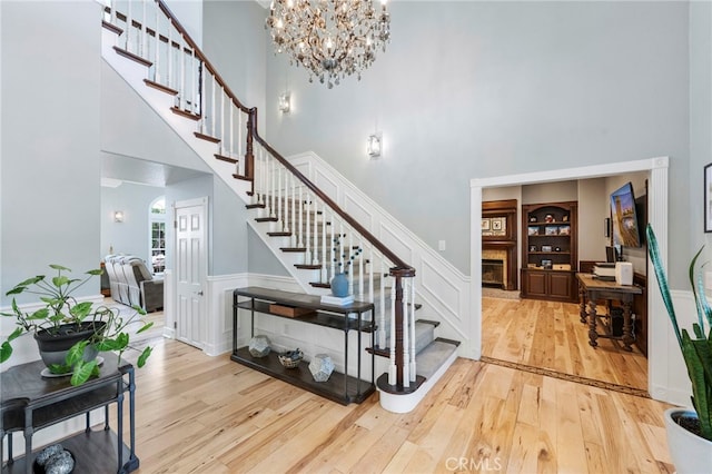 staircase with a fireplace with raised hearth, built in features, hardwood / wood-style floors, a high ceiling, and a chandelier