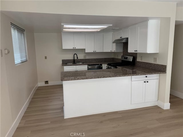 kitchen featuring gas range, dishwashing machine, dark stone countertops, a peninsula, and a sink