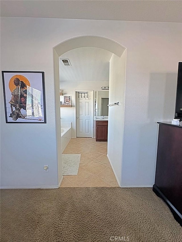 hall featuring light tile patterned floors, baseboards, visible vents, arched walkways, and light carpet