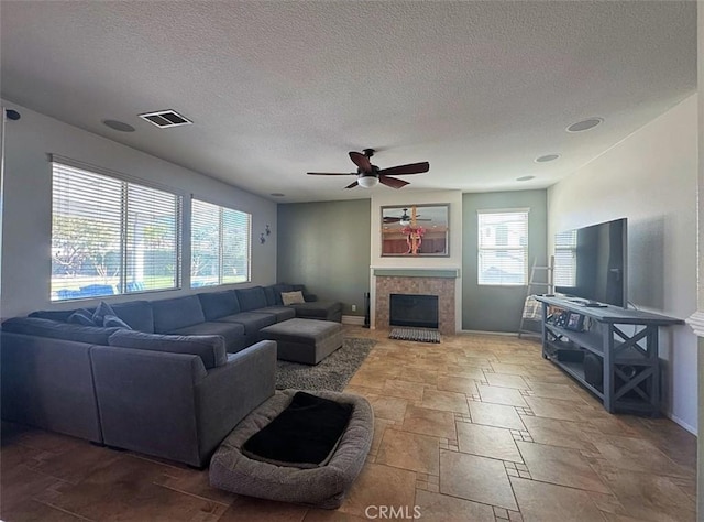 living area featuring visible vents, a textured ceiling, a fireplace, baseboards, and ceiling fan