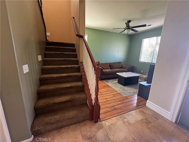 stairs featuring baseboards, ceiling fan, and stone finish floor