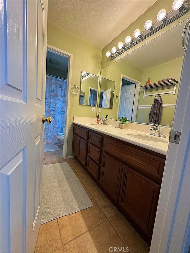 full bathroom with a sink, a textured ceiling, double vanity, and toilet