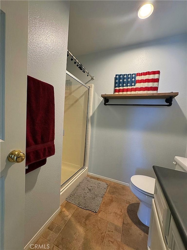 bathroom featuring toilet, a stall shower, stone finish flooring, baseboards, and vanity