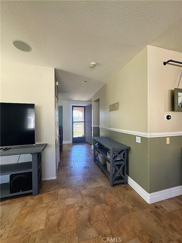 corridor with a textured ceiling, baseboards, and stone tile flooring