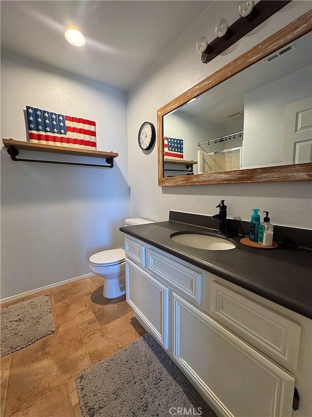 bathroom with visible vents, toilet, stone finish flooring, baseboards, and vanity