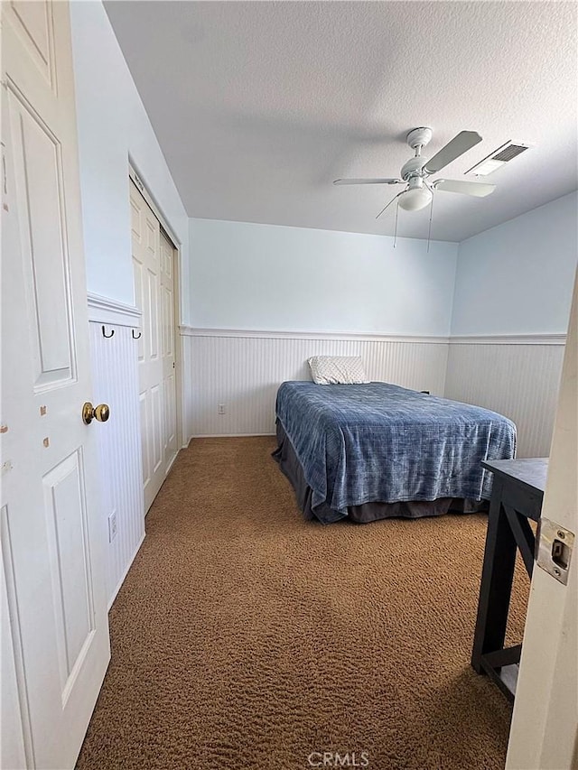 bedroom with a textured ceiling, carpet flooring, visible vents, and wainscoting