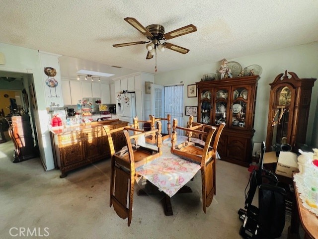 dining room featuring a ceiling fan, light colored carpet, and a textured ceiling