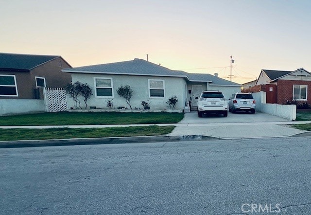 view of front of home featuring stucco siding, a front yard, driveway, and fence