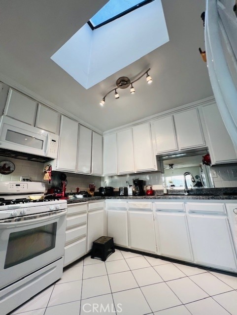 kitchen with dark countertops, white cabinetry, white appliances, a skylight, and decorative backsplash