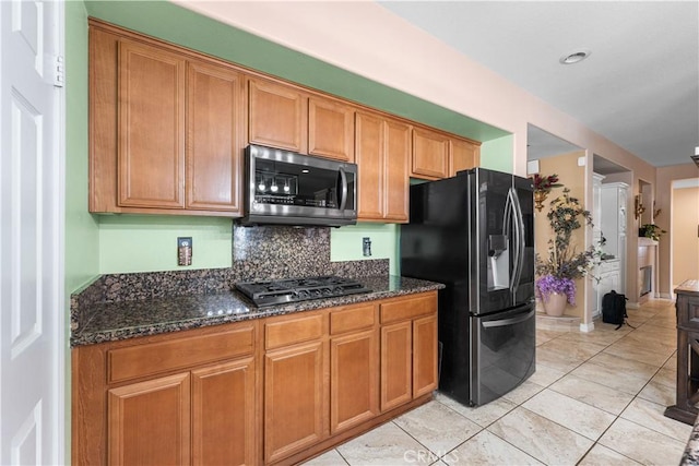 kitchen featuring decorative backsplash, brown cabinets, stainless steel appliances, and dark stone countertops