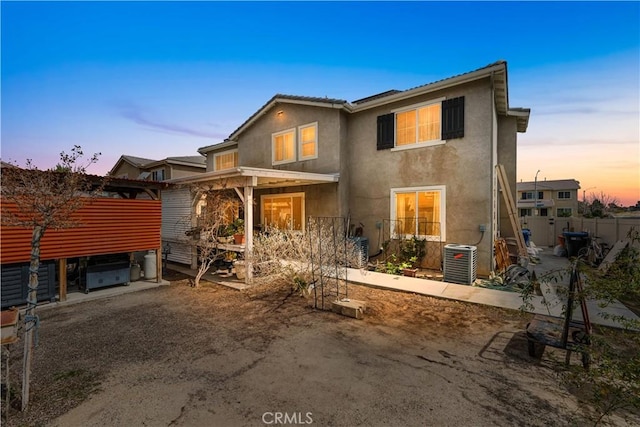 back of house at dusk featuring central AC unit, stucco siding, and fence