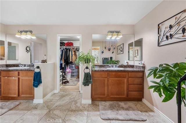 bathroom with a walk in closet, two vanities, and a sink