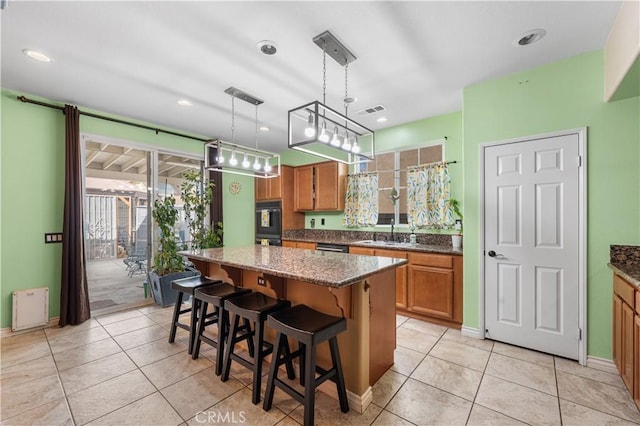 kitchen featuring dark stone countertops, light tile patterned floors, brown cabinetry, and a center island