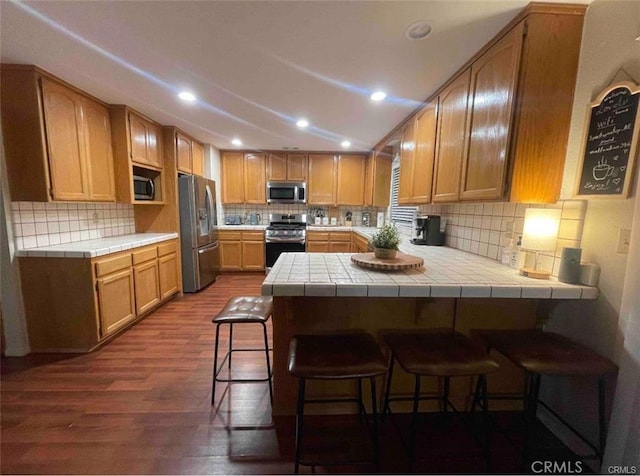 kitchen featuring stainless steel appliances, a peninsula, a breakfast bar, and dark wood-style floors