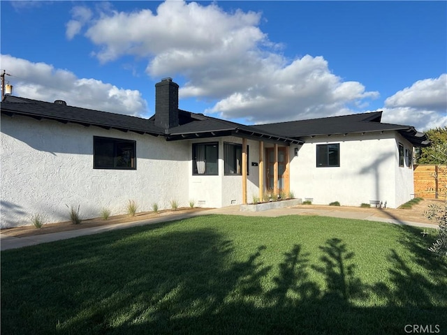 view of front of house with stucco siding, a chimney, and a front lawn