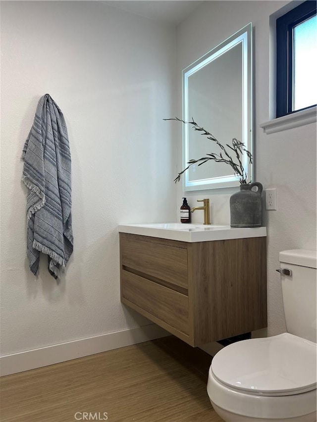 half bath featuring vanity, toilet, wood finished floors, and baseboards