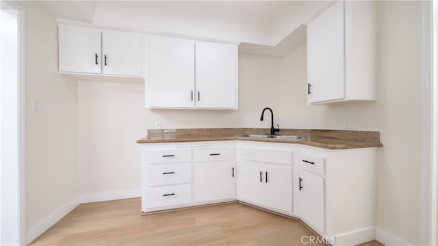 kitchen with a sink, light wood-type flooring, dark stone countertops, and white cabinetry