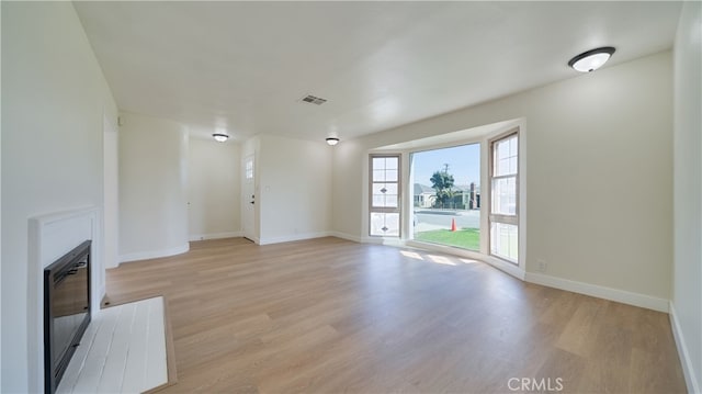 unfurnished living room with a glass covered fireplace, light wood-style flooring, visible vents, and baseboards